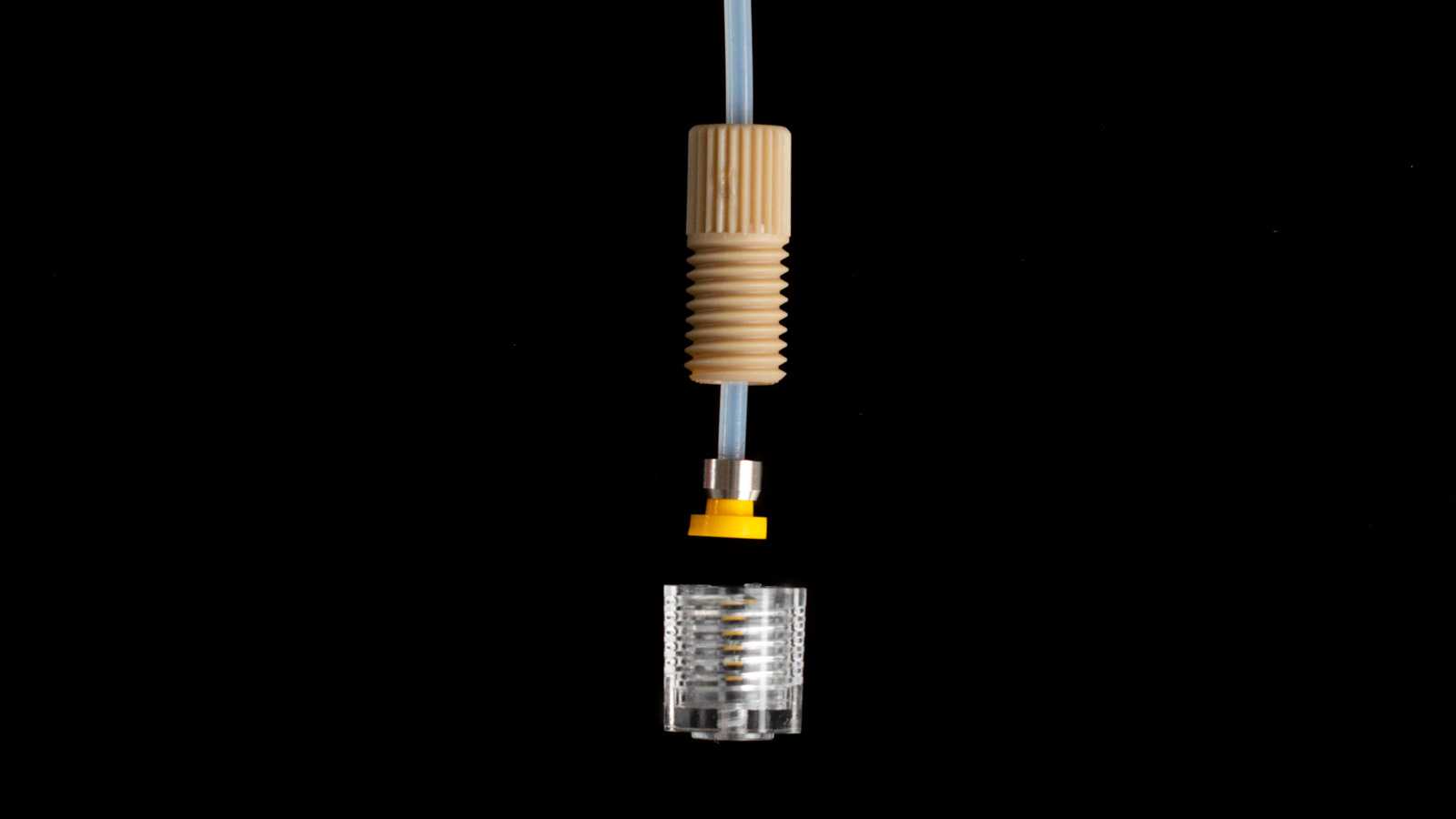 A disassembled super flangeless 1/4-28 capillary tube interface with 1/4-28 port. From top to bottom: tubing, nut, ferrule, and the 1/4-28 port.