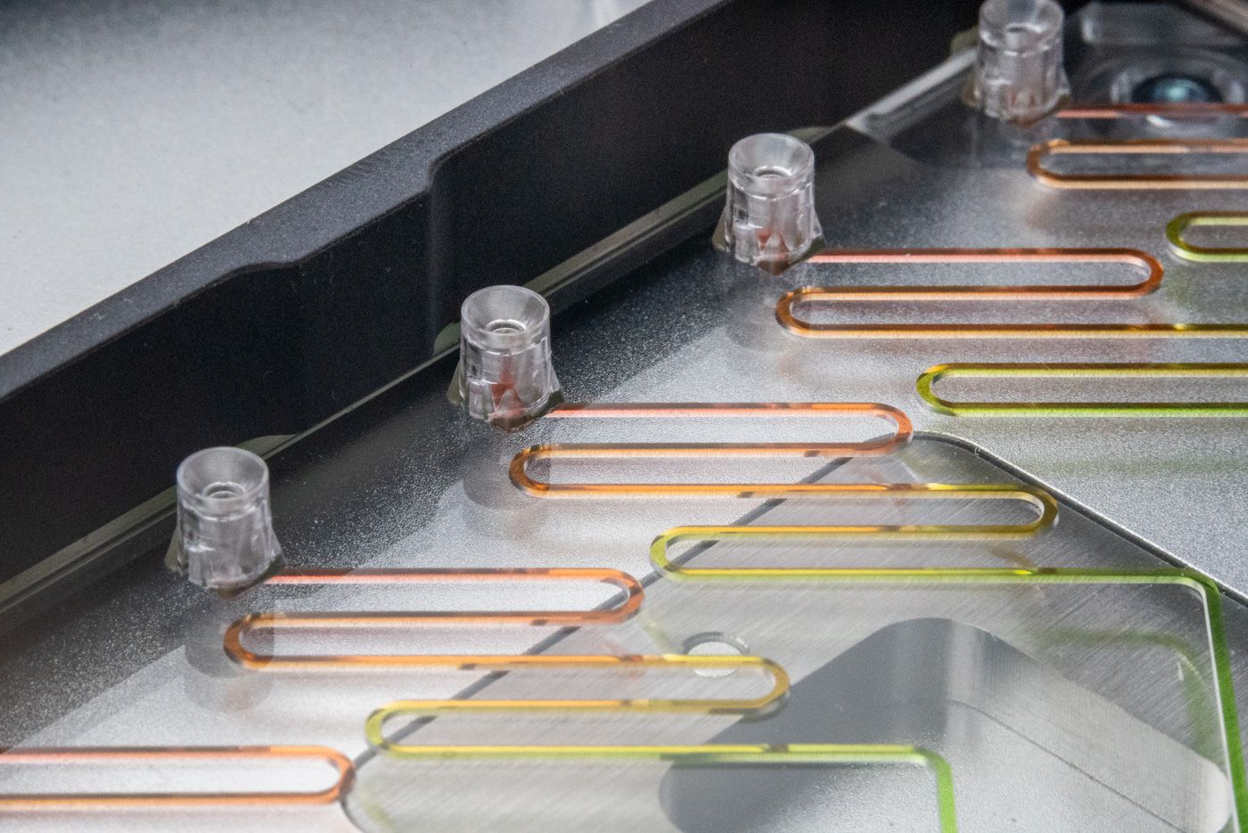 A microfluidic device with an SLAS adapter placed on the deck of an automated liquid handler. The microfluidic device has multiple pipette interfaces along one edge connected to meandering channels filled with multiple colored fluids.