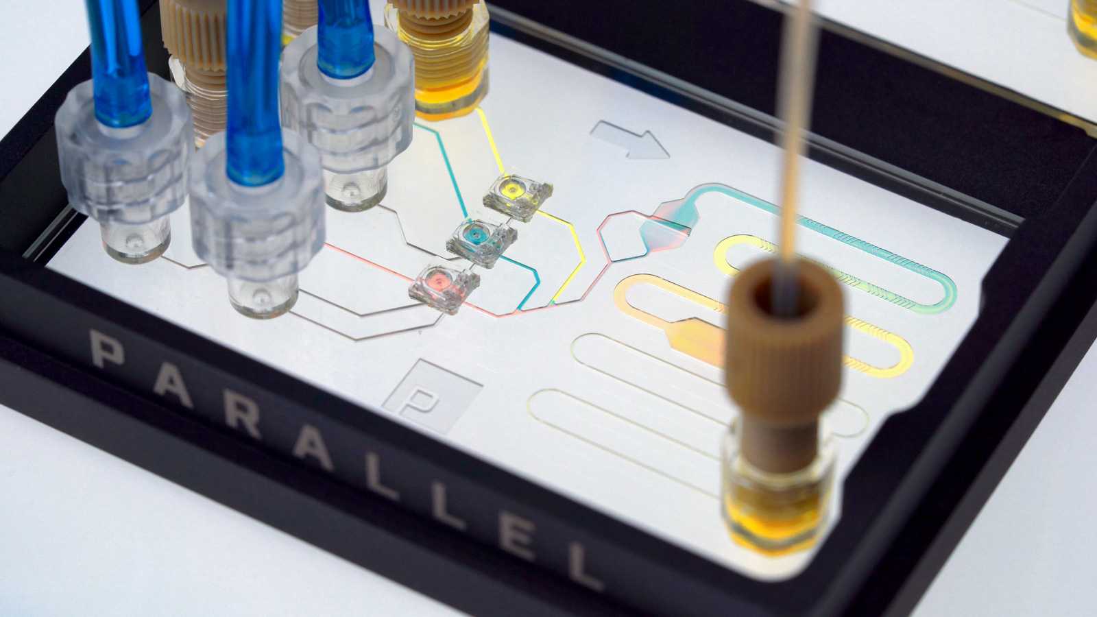 Three MV-1 microvavles mixing pink, blue, and yellow liquids in a double-slide format microfluidic device with three Luer-lock ports and four 1/4-28 ports.